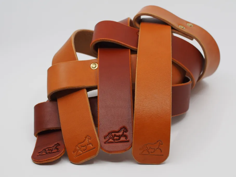 two pairs of straps, one tan with brass and one chestnut with copper, alternate in a stack. both colors are warm and rich, with the chestnut notably ruddier and darker