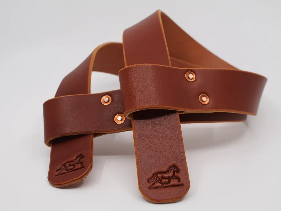 a pair of chestnut lifting straps with horses stamped on the rounded ends. the straps are looped through themselves, forming a 'p' shape. a pair of offset, solid copper rivets hold the loops together.