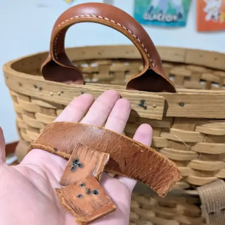 my hand holds a rotted and ruined carrying strap; behind it, a rolled handle sits proudly on a large backpack basket (basketpack?)