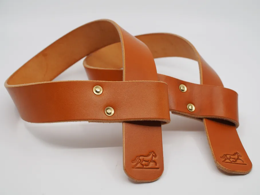 a pair of tan lifting straps with horses stamped on the rounded ends. the straps are looped through themselves, forming a 'q' shape. a pair of offset, solid brass rivets hold the loops together. the shine of the leather grain contrasts with the matter flesh side.